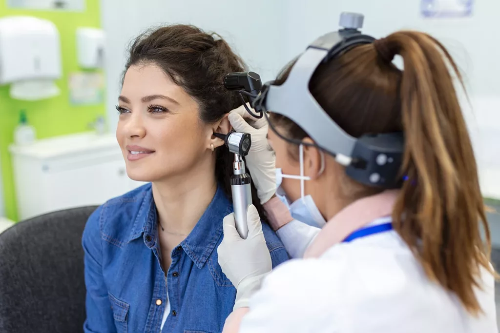 A young adult women in a hearing clinic happily undergoing a hearing exam performed by a hearing care specialist.